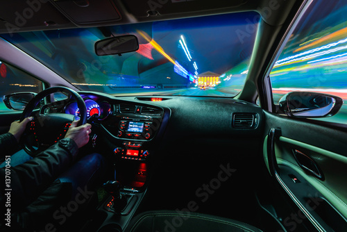 hands on the wheel a car moves at fast speed at the night. Blured road with lights with car on high speed