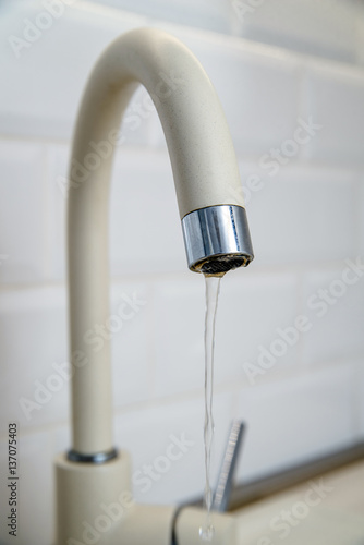 Beige faucet in the kitchen on a background of white tiles 