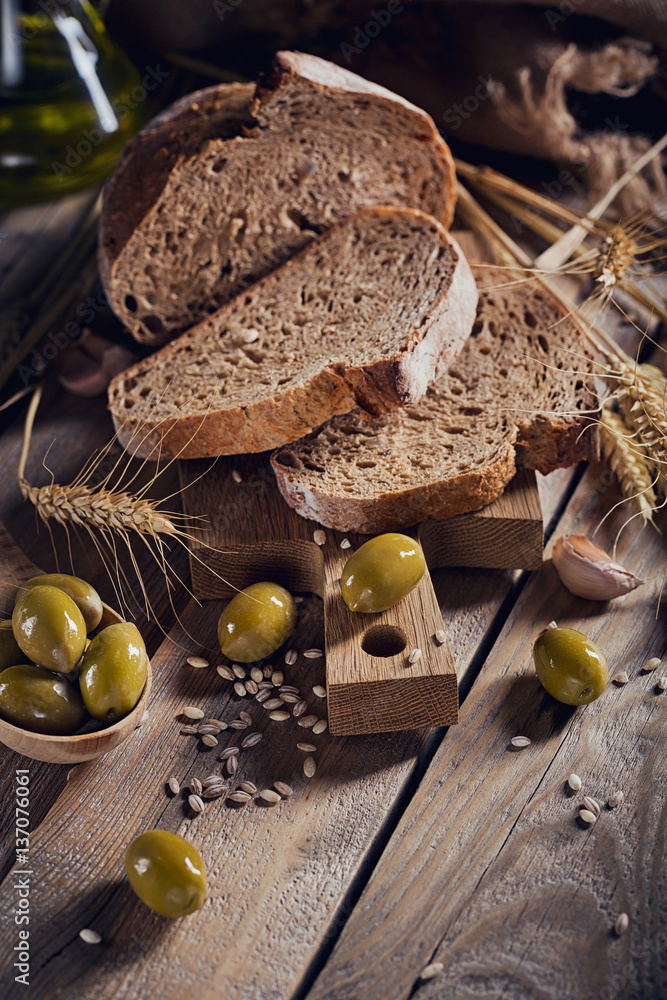 Fresh multigrain crusty bread, green olives and wheat ears on a