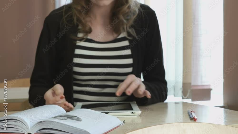 Student sitting at desk looks for important text using silver computer tablet Student sitting at desk looks for important text using silver computer tablet