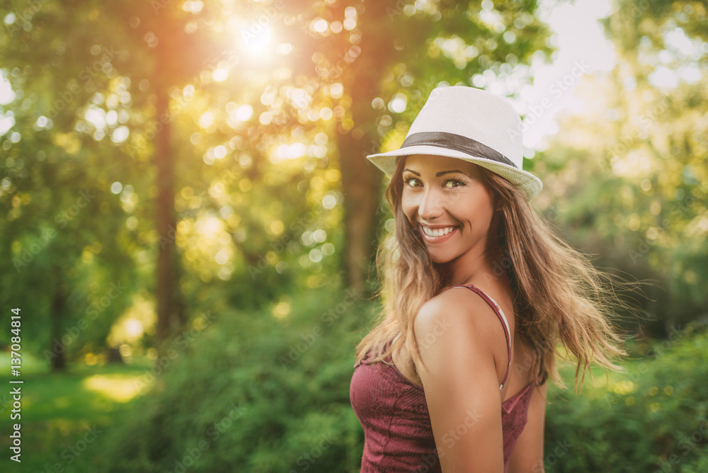 Portrait of a beautiful smiling girl with summer hat in the nature. Looking at camera.