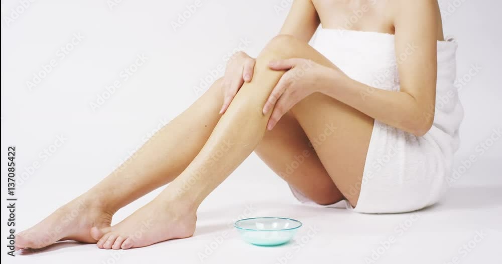 The young woman with perfect body applying refreshing cream/body lotion on her legs ion a white background. Concept of depilation, smooth skin, skincare, cosmetics, wellness center, healthy lifestyle The young woman with perfect body applying refreshing cream/body lotion on her legs ion a white background. Concept of depilation, smooth skin, skincare, cosmetics, wellness center, healthy lifestyle