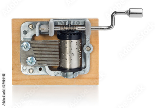Silver music box mechanism with the handle on a wooden plank. Musical toy in the view from the top on a white background with slight reflection.