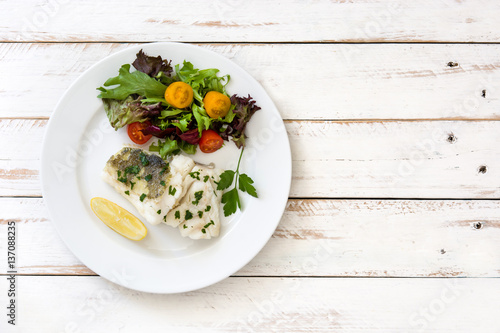 Fried cod fillet and salad in plate on white wooden background.Top view
 photo