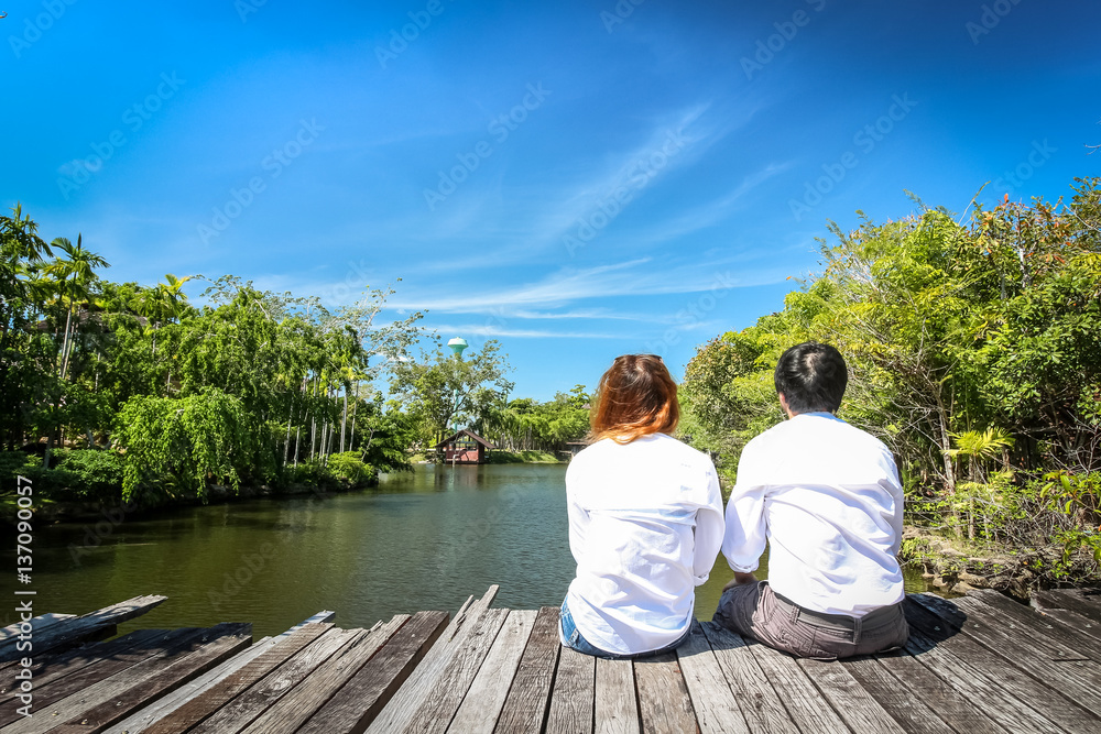 Rear view of couple sitting on wooden bridge over lake