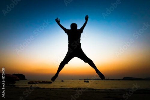 Back view of unidentified silhouette young man jumping over the sea beach with sunset background