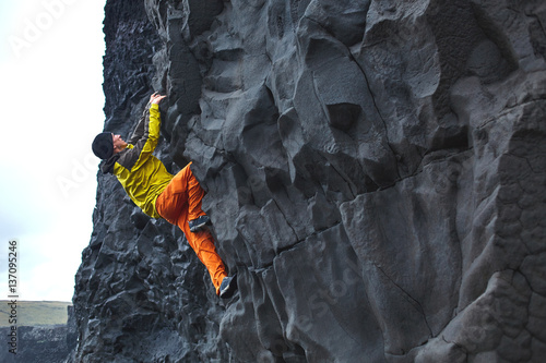 male rock climber. rock climber climbs on a rocky wall on the ocean bank. man makes hard move without rope.