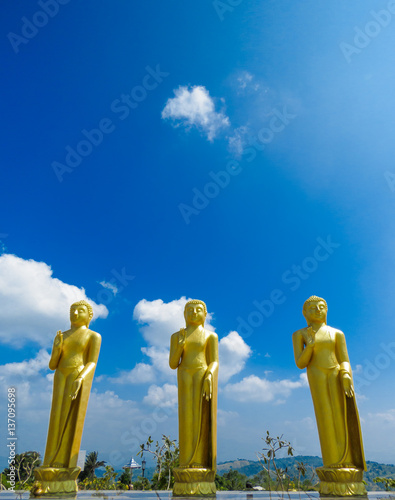 Three Golden standing tall Buddha Statue scluptures with blue sky and clouds at Nelligala International Buddhist Center Kandy, Sri Lanka photo