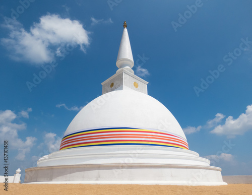 White Stupa Dagabo on sand wrapped with Buddhist flag and blue sky with clouds at Nelligala International Buddhist Center Kandy, Sri Lanka photo