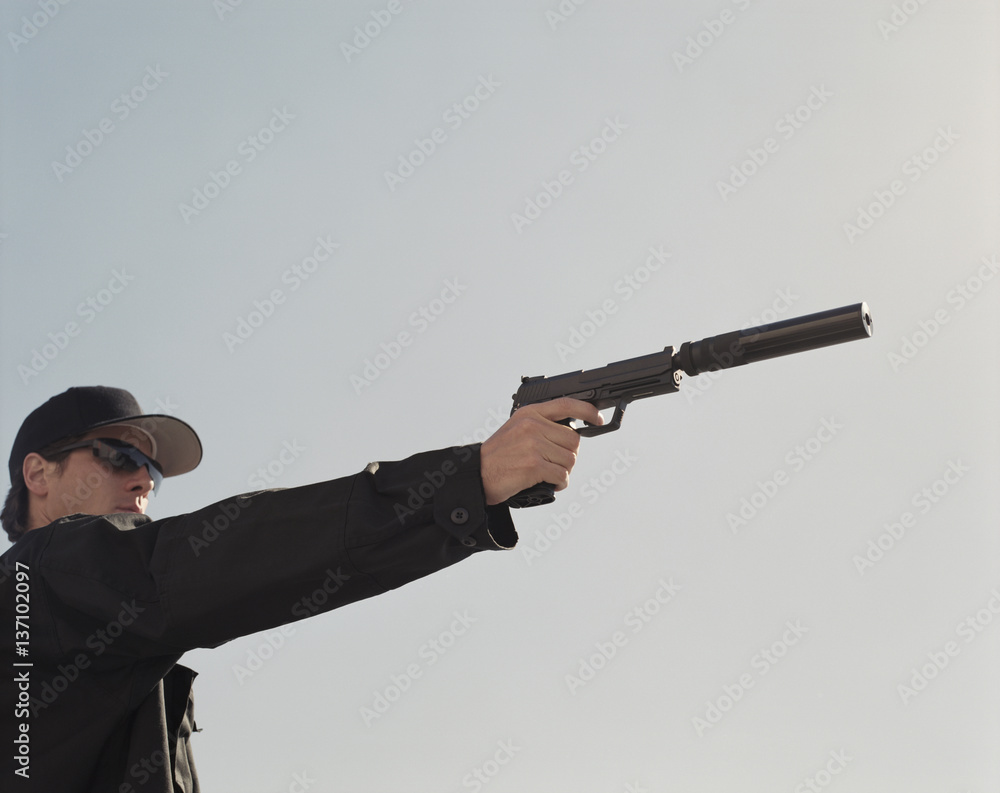 Man in special forces, aiming high powered hand gun with silencer attached Man in special forces, aiming high powered hand gun with silencer attached