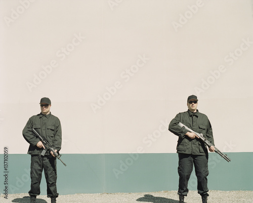 Two men wearing special forces uniforms, holding high powered guns photo