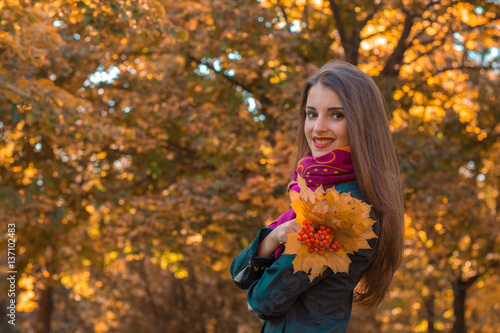 beautiful young girl stands against the backdrop of autumnal trees and smiling