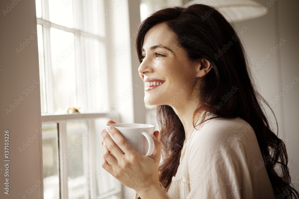 Smiling woman looking out window with coffee Smiling woman looking out window with coffee