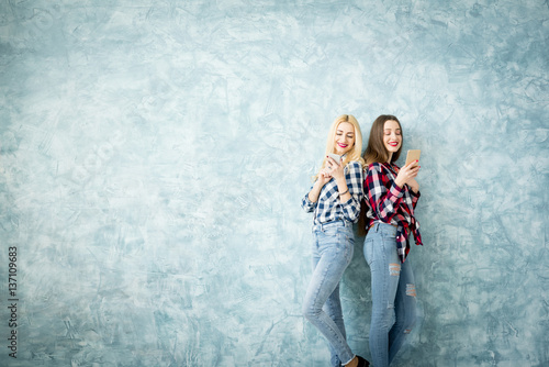 Female friends using smart phones on the blue wall background. Wide shot with copy space