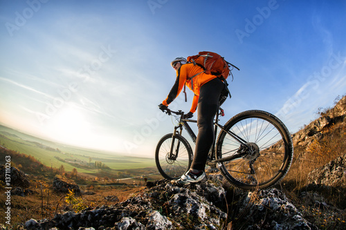 Cyclist man standing on top of a mountain with bicycle and enjoying valley view on a sunny day against a blue sky
