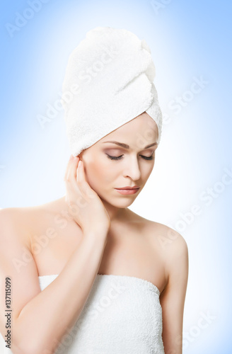 Portrait of young, beautiful woman with bath towel on her head: over blue background. Healthcare, spa, makeup and face lifting concept.