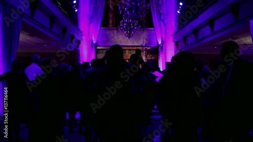 Group of silhouetted people dancing in a dark banquet hall for a wedding reception.