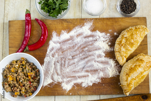 Empanadas cooking preparations: flour with spices, culinary herbs and minced pork on wood board