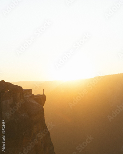 Person standing on edge of cliff at sunset 
