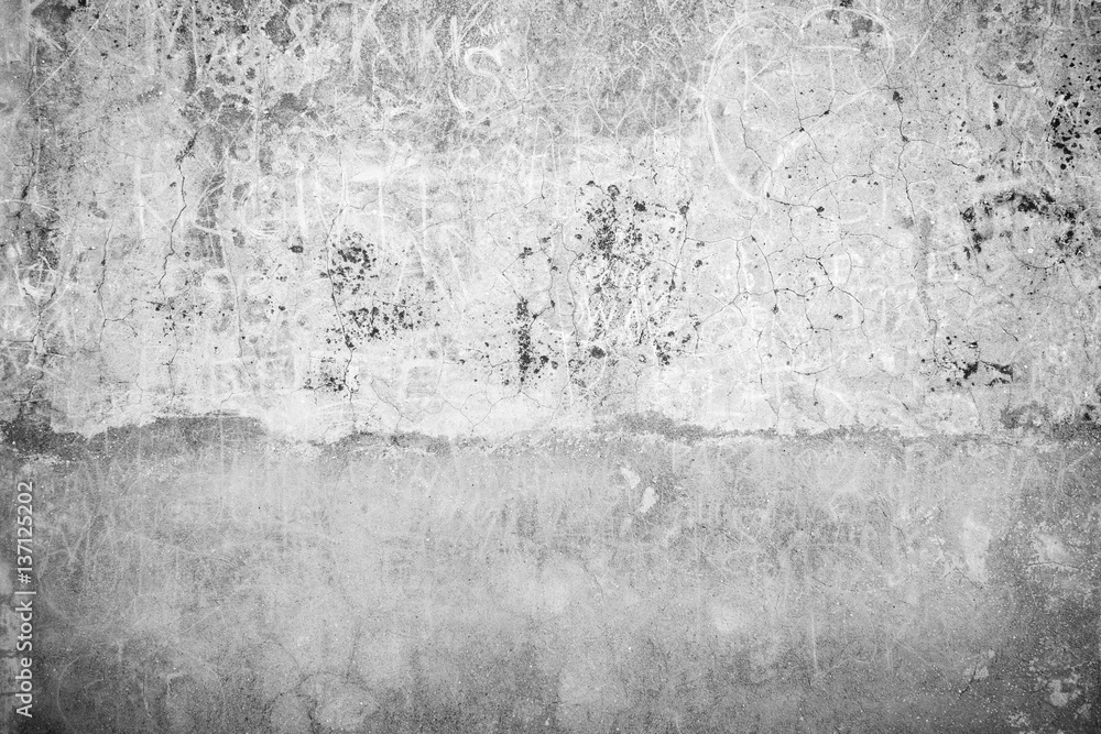 Weathered, aged and cracked gray stone wall with names scratched on it in black&white.