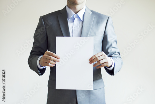 Photo of a businessman wearing light grey suit holding blank paper 