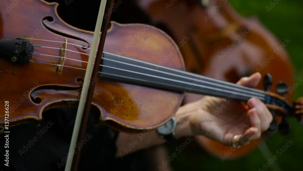 Close up of two women playing a violin and a cello outdoors. Close up of two women playing a violin and a cello outdoors.