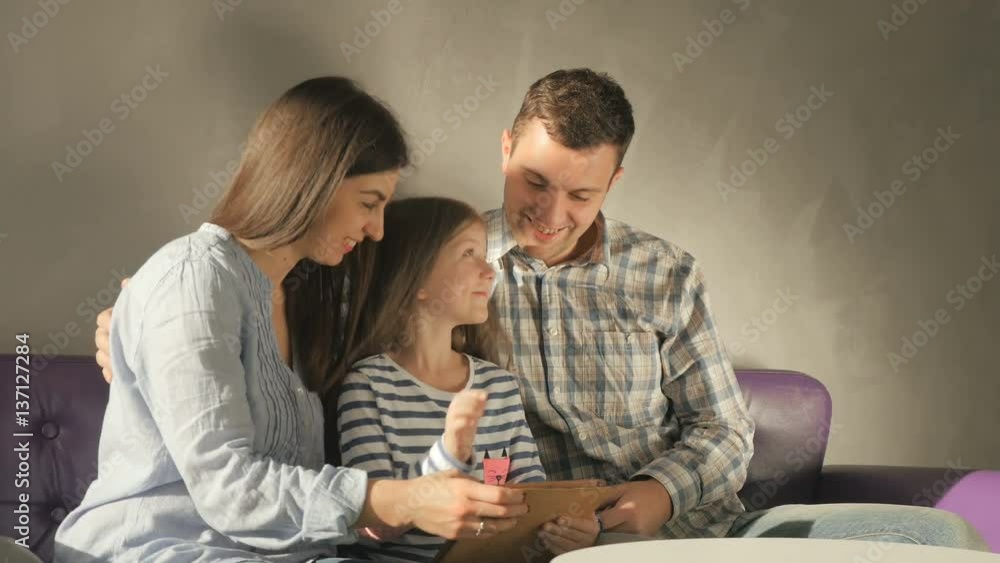 Mother, father and daughter using the tablet on the purple sofa in the room Mother, father and daughter using the tablet on the purple sofa in the room