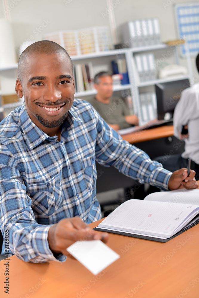 Man at desk holding forward a blank business card Man at desk holding forward a blank business card