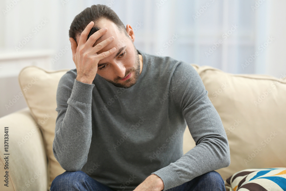 Handsome depressed man sitting on sofa at home Handsome depressed man sitting on sofa at home