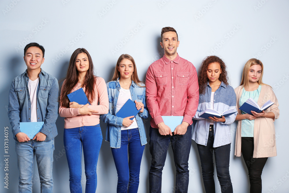 Group of people with books standing near light wall Group of people with books standing near light wall