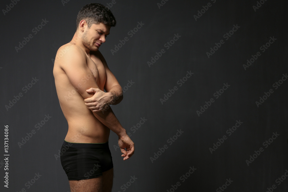 Young man suffering from pain in elbow on dark background Young man suffering from pain in elbow on dark background