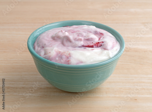 Raspberry yogurt in a small bowl on a wood table.