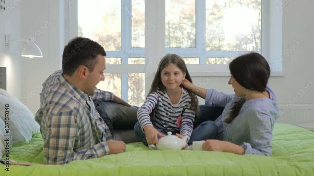 Young parents playing with their little daughter on a big bed in the bedroom Young parents playing with their little daughter on a big bed in the bedroom