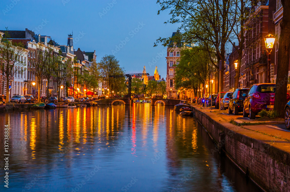 Traditional old buildings and boats at night in Amsterdam, Netherlands.