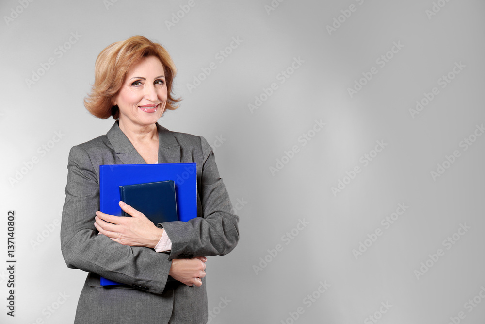 Attractive senior woman holding folder on grey background Attractive senior woman holding folder on grey background