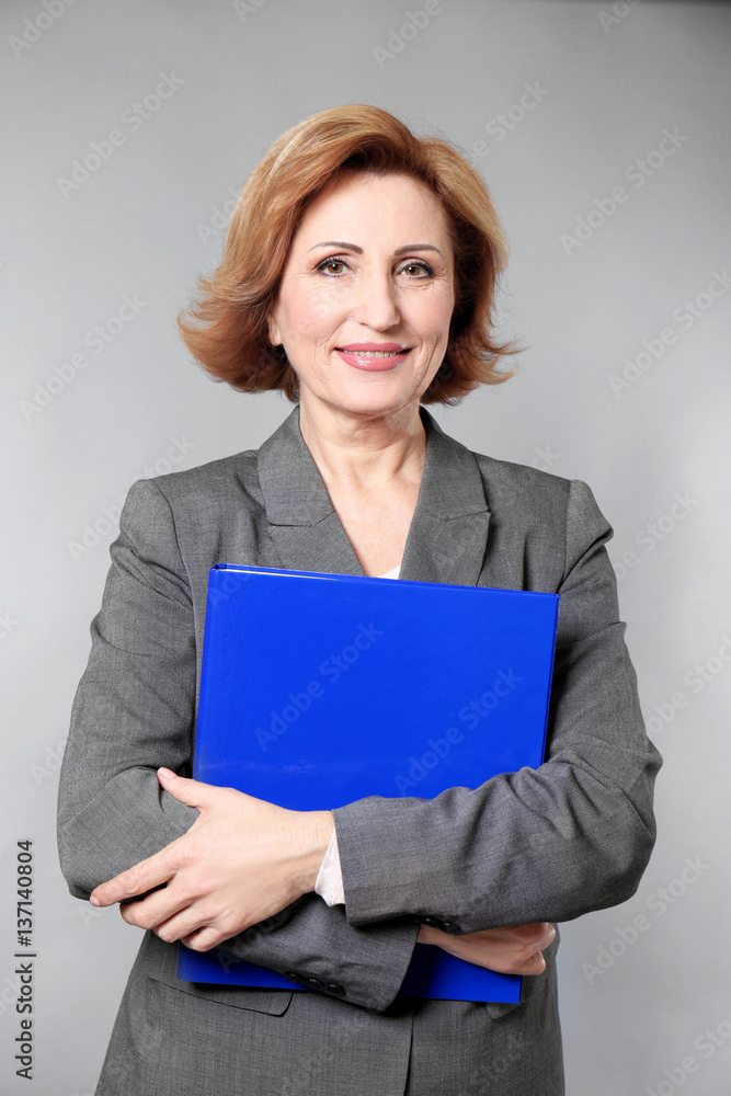 Attractive senior woman holding folder on grey background Attractive senior woman holding folder on grey background