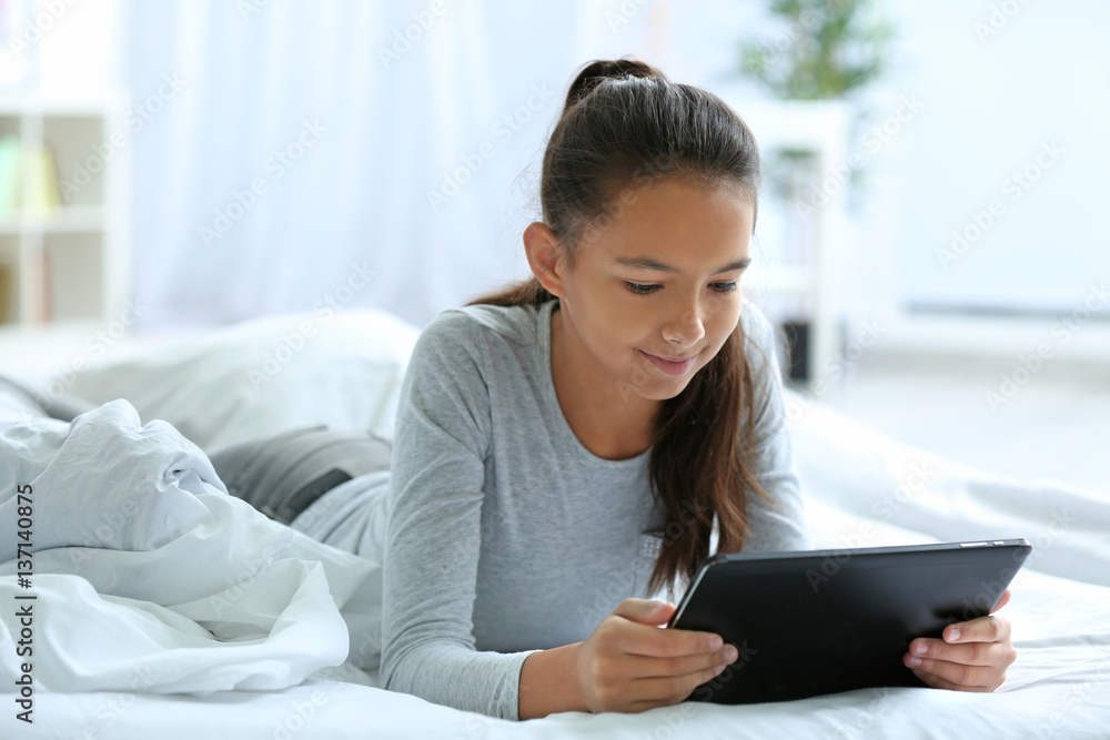 Cute girl lying on bed with tablet computer Cute girl lying on bed with tablet computer