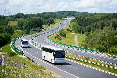 White buses driving on the highway winding through forested areas. View from above.