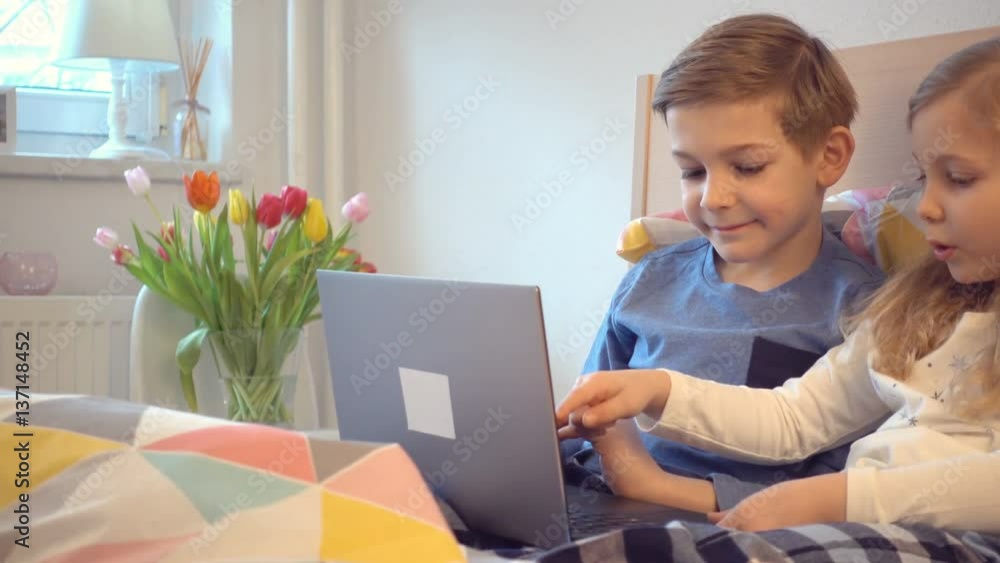 Two happy children having fun with laptop in bed Two happy children having fun with laptop in bed