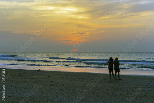Two women on the beach looking at sunrise.