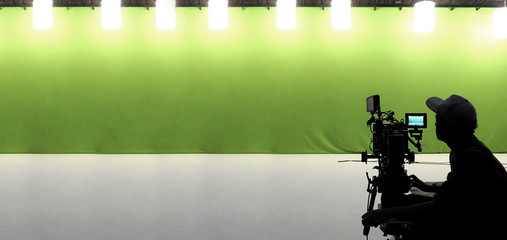 Silhouette of camera man with his professional video kit such as high definition lens equipment, tripod, rig, gimbal, LED monitor and green screen for chroma key technique in studio panorama view.