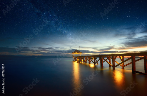 Beautiful night seascape with milky way in the sky and pier stretching into the ocean.