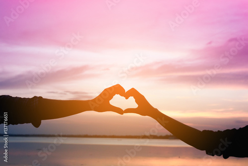 Silhouette of hands in shape of love heart at the sunset