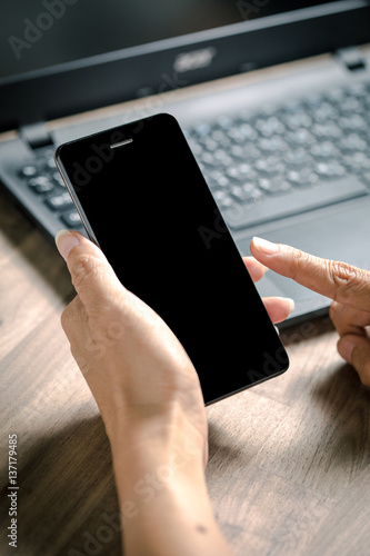 Business women hand holding smart phone to working with laptop