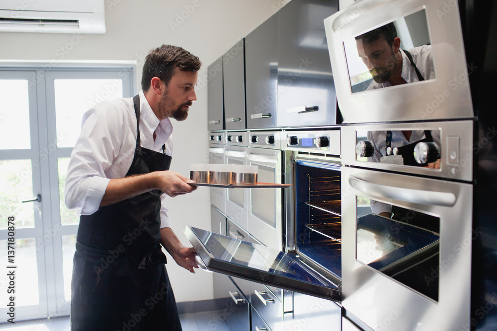 Chef putting tray into the oven. Chef putting tray into the oven.
