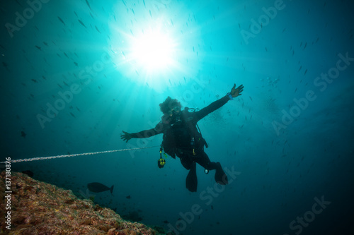 Silhouette of man scuba diver between water surface and sea bottom