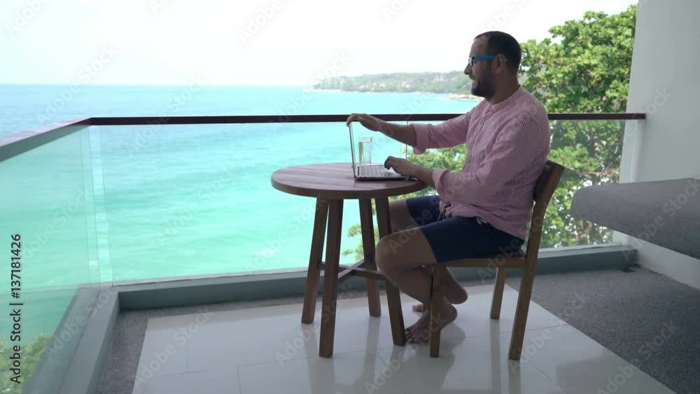 Man finishing working on laptop, stretching arms and drinking water on terrace
Man finishing working on laptop, stretching arms and drinking water on terrace