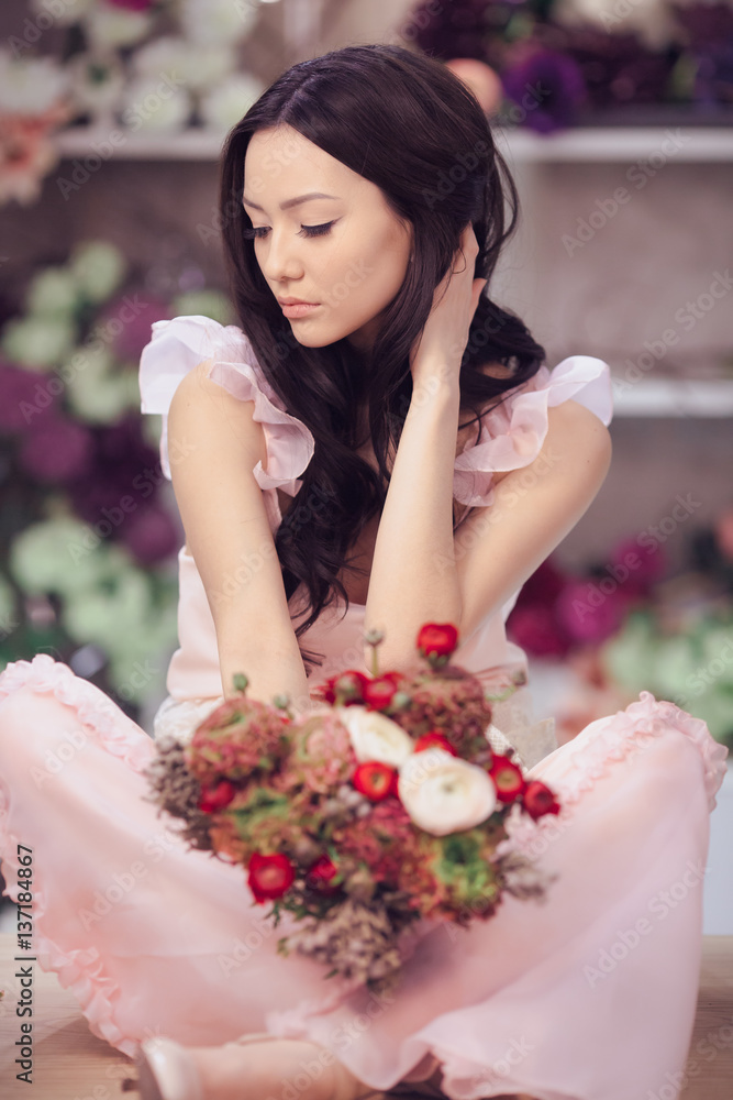 Beautiful asian woman florist in pink dress with bouquet of flowers in hands in flower store Beautiful asian woman florist in pink dress with bouquet of flowers in hands in flower store
