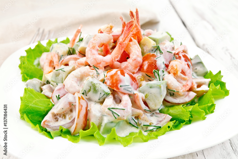 Salad with shrimp and avocado in white plate on board