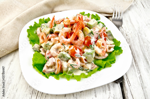 Salad with shrimp and avocado in white plate on light board